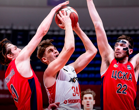 Баскетбольный матч: игрок в белой форме пытается забросить мяч в кольцо, двое игроков в красной форме команды ЦСКА пытаются его блокировать. Напряжённый момент игры