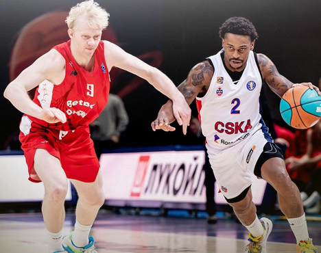 Два баскетболиста в движении на площадке: игрок в красной форме противостоит игроку в белой форме. У второго игрока в руках мяч, и он пытается обойти соперника. На заднем плане размыт логотип в зале